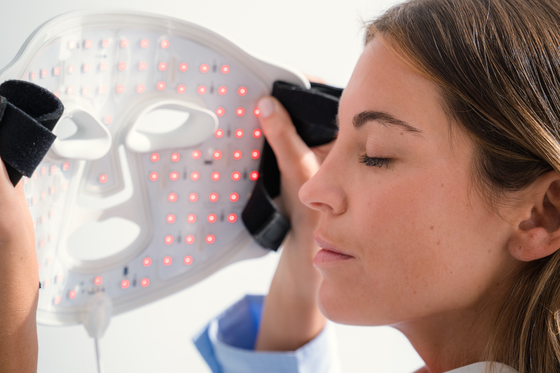SKINVITY SILICONE LED MASK SE VEN LOS FOCOS DE LUZ LED ROJA INTERIORES Y LA FORMA DE LA MÁSCAR, LA MISMA QUE ES SOSTENIDA POR UNA MUJER